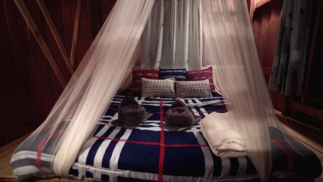 Spacious comfy bed with mosquito net on wooden platform in cozy cabin.