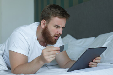 Naklejka premium Nervous sad upset confused young man, stressed worried guy having problem with paying, buying online, payments with credit blocked bank card, looking at screen, monitor of laptop. Internet fraud