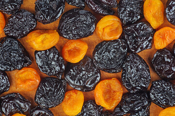 Dried plums and apricots on wooden background.