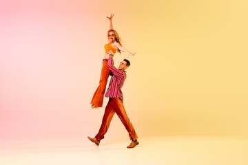 Performance. Beautiful, emotional young people, man and woman in vintage, stylish clothes dancing over gradient pink yellow background. Concept of retro style, dance, fashion, art, hobby, music, 70s
