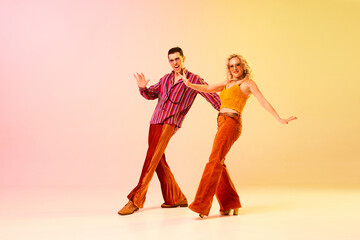 Expressive, talented, emotional couple, man and woman in stylish clothes dancing disco dance against gradient pink yellow background. Concept of retro style, dance, fashion, art, hobby, music, 70s