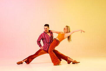 Fototapeta na wymiar Excitement. Artistic, expressive couple, man and woman emotionally dancing disco dance against gradient pink yellow background. Concept of retro style, dance, fashion, art, hobby, music, 70s