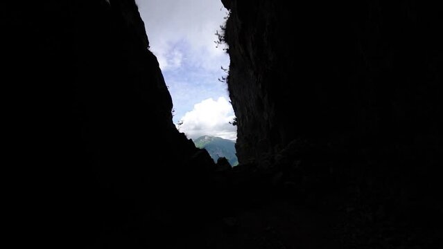 Entrance to dark cave on steep cliff against sky with clouds