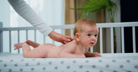 Small naked newborn caucasian baby boy lies on his stomach while mother's hands massages his small back and develops muscles. Healthy baby concept
