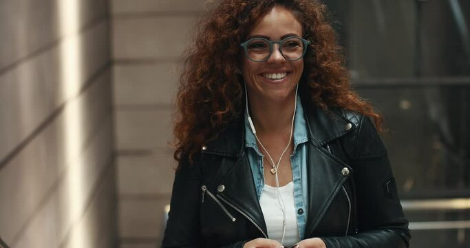 Stylish young woman smiling and listening to music on her cellphone while riding up a metro station escalator 
