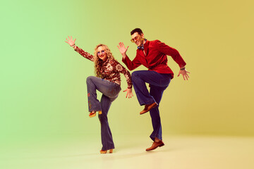 Young handsome man and beautiful woman in stylish retro clothes dancing against gradient green...