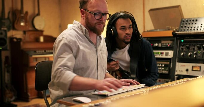 Young African American guitarist and music producer working on a track together during a session in a recording studio