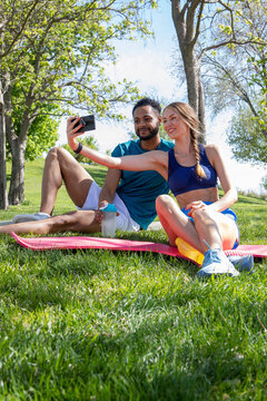 young multiethnic couple, dressed in sportswear, taking photos with their mobile phone, while taking a break from their training, healthy lifestyle concept,