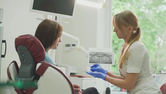The dentist consults the patient and shows the woman Invisalign braces, transparent plastic removable aligners. Dentistry, dental clinic, orthodontics.