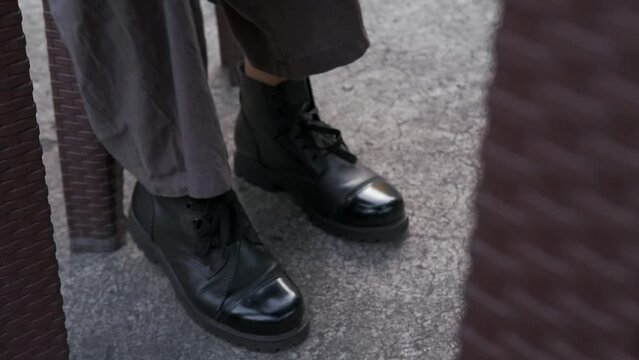 Close up of woman uncrossing leg and then shaking foot impatiently, wearing shiny black boots