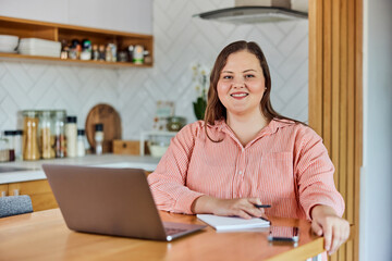 Portrait of a curvy businesswoman working over the laptop at home.