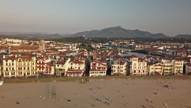 Rising aerial dolly above golden sandy beach and cute white and brown coastal buildings near canal