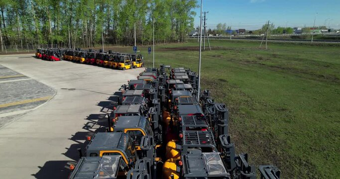 New Jac forklifts parked in a row for sale in a distribution center. Aerial shot. Forklifts in an open-air warehouse. Sale of new Industrial equipment.