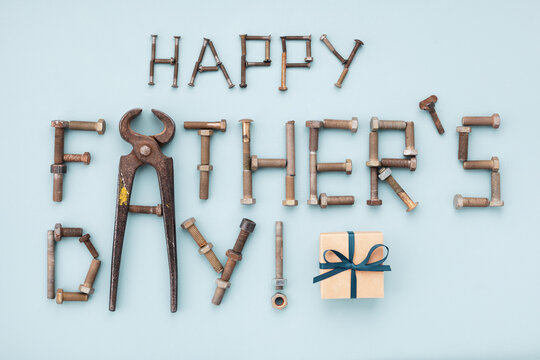 Happy fathers day greeting card with tools and lettering text from vintage screws with gift box top view on blue background.