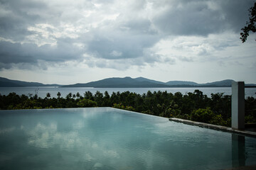 Wide angle view of a beautiful infinity pool in a tropical island overlooking the sea and other islands of exotic archipelago. Overcast day, almost sunset, water reflections.