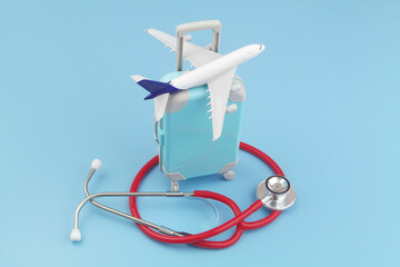 Airplane model on travel suitcase and red stethoscope on blue background.
