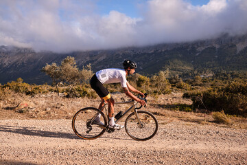 Fototapeta na wymiar Cyclist practicing on gravel road.Fit male cyclist riding a gravel bike on a gravel road with a view of the mountains, Alicante region of Spain