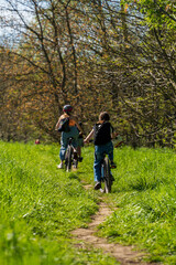 Naklejka premium Group of children riding their bikes on a dirt trail on a sunny spring day among green grass, bike ride, children cycling in the woods, healthy lifestyle, authentic sustainability