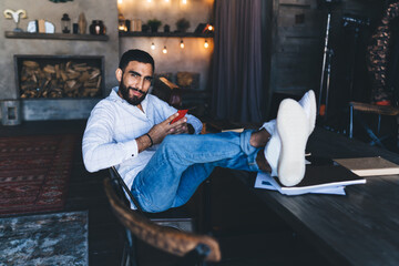 Ethnic man sitting with feet up on table using phone