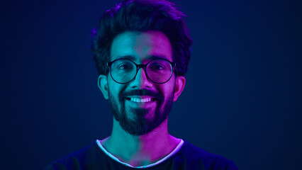 Portrait Indian man Muslim guy developer coding worker smile computer internet technology hacker Arabian male in glasses smiling neon blue ultraviolet studio background high-tech future cyberspace