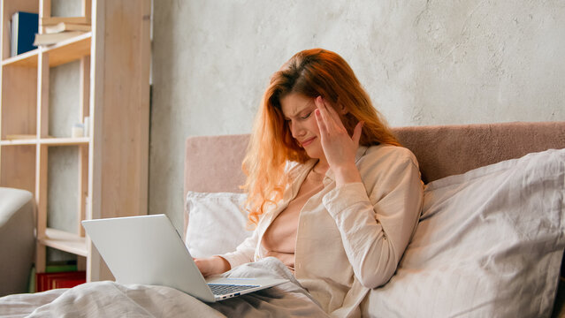 Freelancer Caucasian sick woman working remote from home bed bad feeling headache. Ill student girl studying distant with laptop in bedroom suffer with painful head fever migraine tired with computer