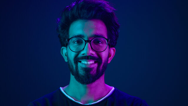 Portrait Indian man Muslim guy developer coding worker smile computer internet technology hacker Arabian male in glasses smiling neon blue ultraviolet studio background high-tech future cyberspace