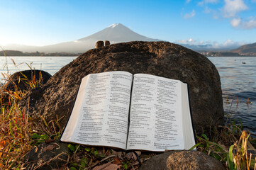 Holy Bible open to Psalms 121, 122, 123 and 124 leaning against a rock on the shore of Lake...
