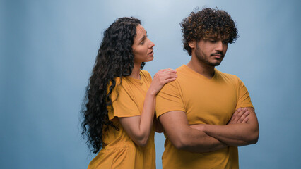 Offended Arabian man Indian husband boyfriend ignoring Latino Hispanic woman wife girlfriend asking forgiveness apologizing after quarrel conflict guilty saying sorry apology at studio blue background - obrazy, fototapety, plakaty