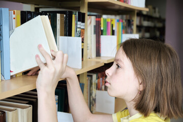 Schoolgirl choosing book in school library. Back to school