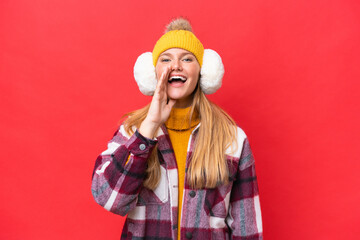 Young beautiful woman wearing winter muffs isolated on red background shouting with mouth wide open