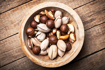 Dried mixed nuts in wooden bowl closeup. Macadamia, Pecan and Brazil nuts with knife on wooden table. Studio macro shoot. Food photography