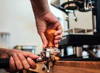 Close-up of hand Barista cafe making coffee with manual presses ground coffee using tamper at the coffee shop