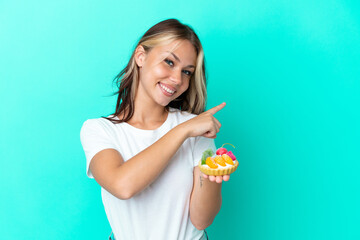 Young Russian woman holding a fruit sweet isolated on blue background pointing back