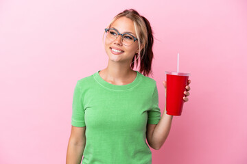 Young Russian woman holding a refreshment isolated on pink background looking to the side and smiling