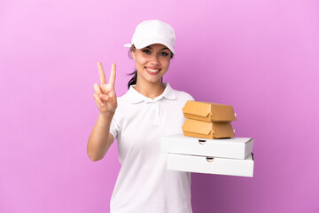 Pizza delivery Russian girl with work uniform picking up pizza boxes and burgers isolated on purple...