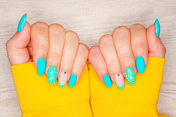 Turquoise nail art female manicure on a light wooden background. Long almond-shaped nails. Close-up of a woman's hands with a delicate manicure on her nails