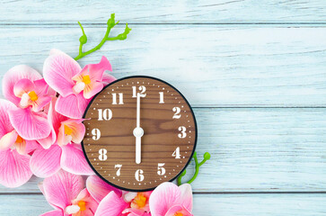The Wooden Alarm clock and pink streaked orchid flower on blue wooden background.