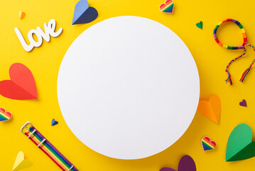 Vibrant yellow backdrop with top view parade accessories flat lay, including rainbow colored hearts, inscription love, wristlet, and pin badges with an empty circle for text or advert