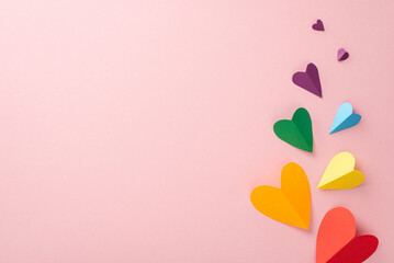 A bright LGBT Pride Month top-down view with rainbow colored paper hearts, on a pastel pink background, with a blank space for text or promotional purposes