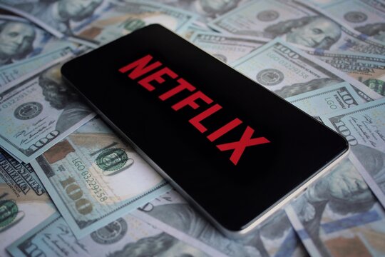 Netflix logo displayed on smartphone on top of pile of money.
