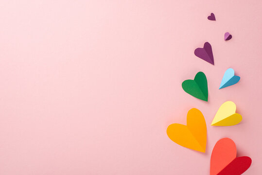 A bright LGBT Pride Month top-down view with rainbow colored paper hearts, on a pastel pink background, with a blank space for text or promotional purposes