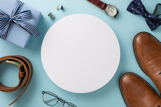 Suave Father's Day Concept. Overhead Shot Of Card, Wrapped Gift, Leather Shoes, Bow-tie, Wristwatch, Accessories, Belt, Cufflinks, Spectacles On Blue Background With Empty Circle For Ad Or Text