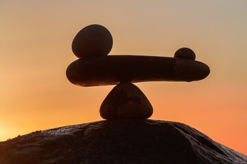 im Gleichgewicht der Kräfte - natürliche Wage aus Steinen am Meer zum orangenen Sonnenuntergang -...