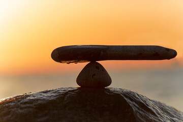 im Gleichgewicht der Kräfte - natürliche Wage aus Steinen am Meer zum orangenen Sonnenuntergang - Symbolfoto	
