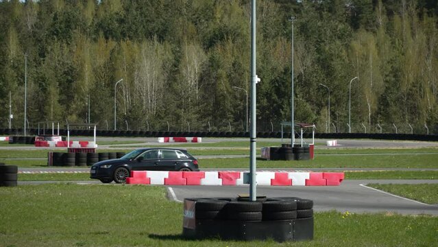 On racing country track, civilian sports cars move interestingly in different directions on different sections. Free races of amateurs on sunny day. Lighting poles christened with tires for safety.