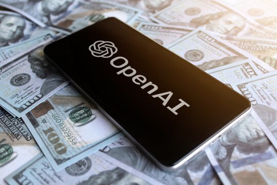 OpenAI logo displayed on smartphone on top of pile of money.