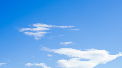 A peaceful cloudscape of fluffy white clouds stretching across a clear blue sky, displaying the beauty and atmosphere of natural environment.