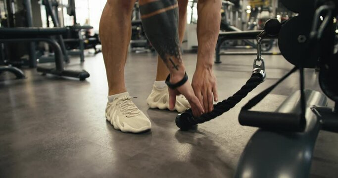 A young man with a naked torso and a tattoo approaches a special simulator in order to perform an exercise that strengthens his back