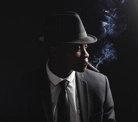 Fototapeta na wymiar Man, gangster and cigarette in studio by dark background with smoke, silhouette and dangerous in shadow. Mafia, secret agent or male in night for smoking with vintage aesthetic by black backdrop