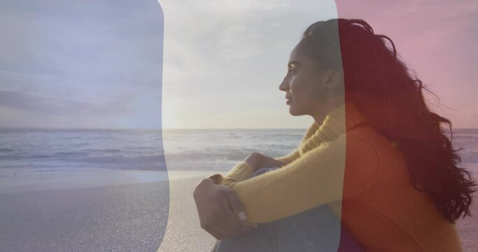 Animation of flag of france over biracial woman sitting at beach